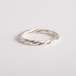 May include: A polished silver ring featuring a continuous twisted rope design. The band has a uniform metallic texture with reflective surfaces that catch the light, creating a series of subtle highlights and shadows along the circular metal structure.
