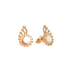 May include: A pair of gold-colored stud earrings. Each earring features a central white, oval-shaped stone surrounded by small, gold-colored beads. The design includes three curved, gold-colored prongs extending upwards.