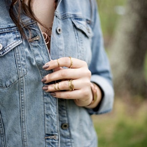May include: A close-up of a person's hand wearing multiple gold rings. The hand is wearing a denim jacket.