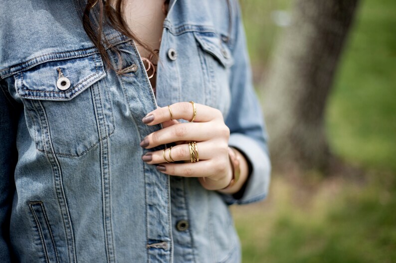 May include: A close-up of a person's hand wearing multiple gold rings. The hand is wearing a denim jacket.