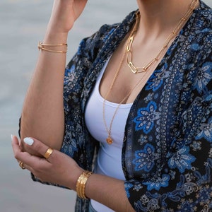 May include: A woman wearing a white tank top and a blue and black floral kimono with gold chain necklaces and bracelets.