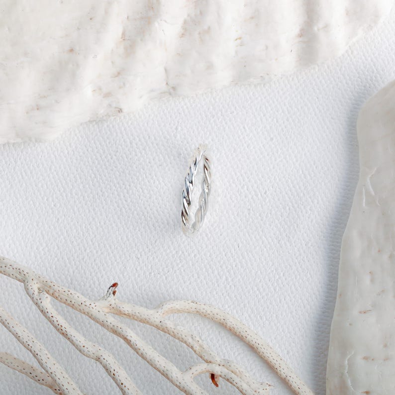 May include: A silver ring featuring a twisted, rope-like texture. The band has a polished, metallic finish and a continuous, uniform design that wraps around the entire circumference of the ring, creating a subtle, spiraling pattern.