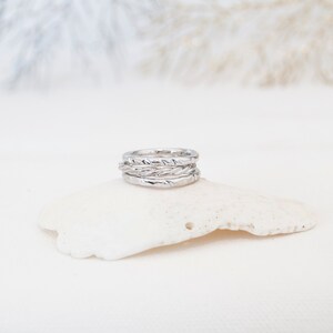 May include: A set of four silver rings stacked on top of each other. The rings are all different widths and have a textured surface.