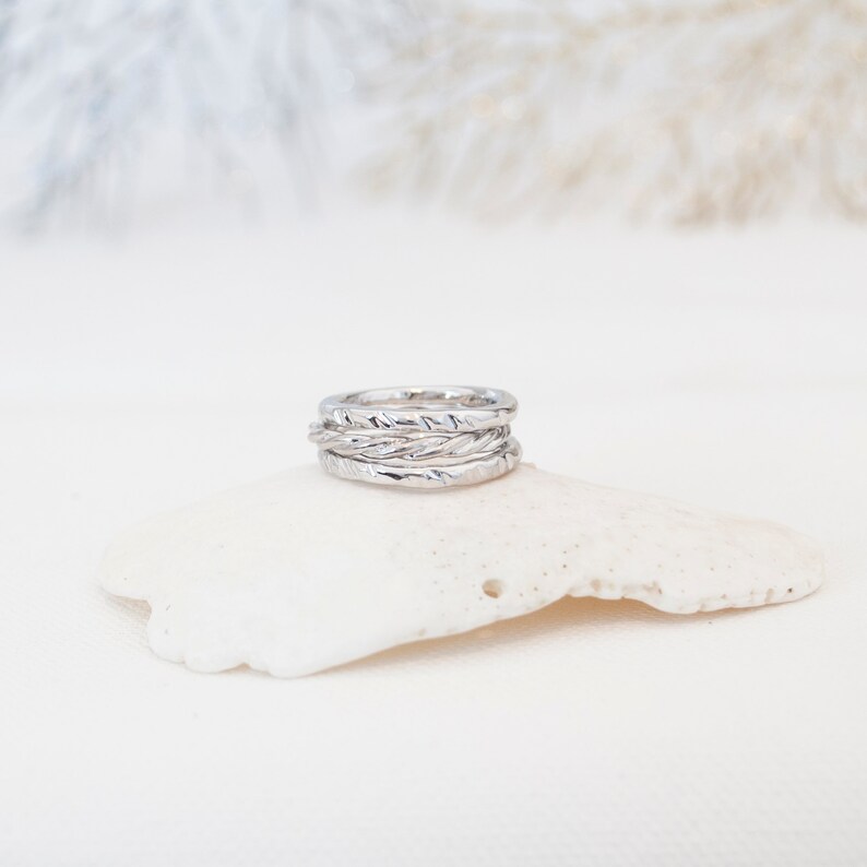 May include: A set of four silver rings stacked on top of each other. The rings are all different widths and have a textured surface.