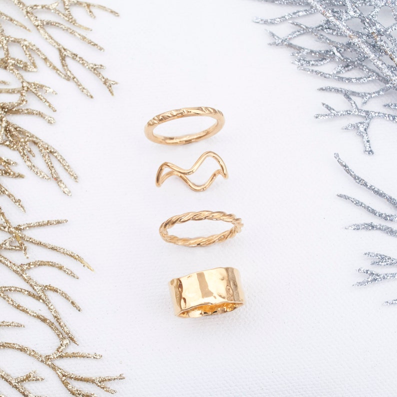 May include: Four gold-toned rings, each with a different design. The rings are arranged vertically on a white background.