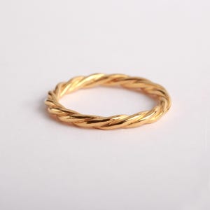 May include: A gold-colored ring with a twisted rope-like texture. The band features a continuous spiral pattern that creates a series of small, uniform ridges along the entire circumference of the circular metal jewelry piece.