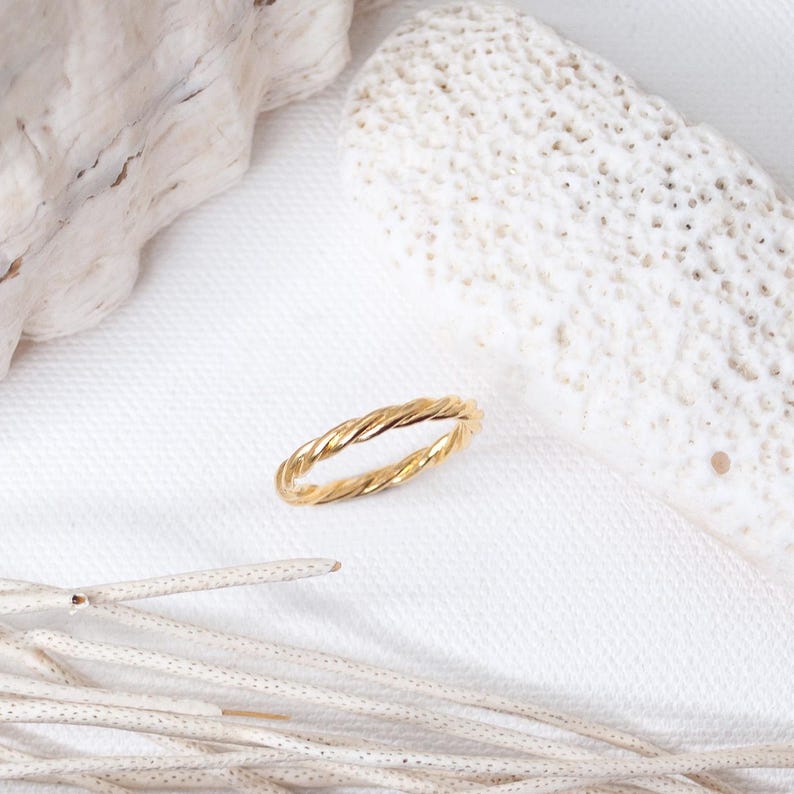 May include: A gold-toned ring featuring a twisted, rope-like design. The band has a continuous spiral texture that creates a series of small, uniform ridges along the entire circumference of the circular metal jewelry piece.