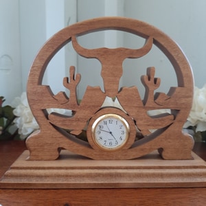 May include: Wooden clock with a carved design of a longhorn steer and cacti. The clock face is round and has gold-colored hands and numbers.