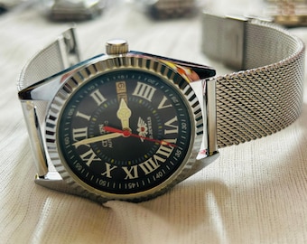 May include: A silver-toned Citizen automatic watch with a black face, Roman numeral hour markers, and a date display at the 3 o'clock position. The watch has a mesh band and a fluted bezel.