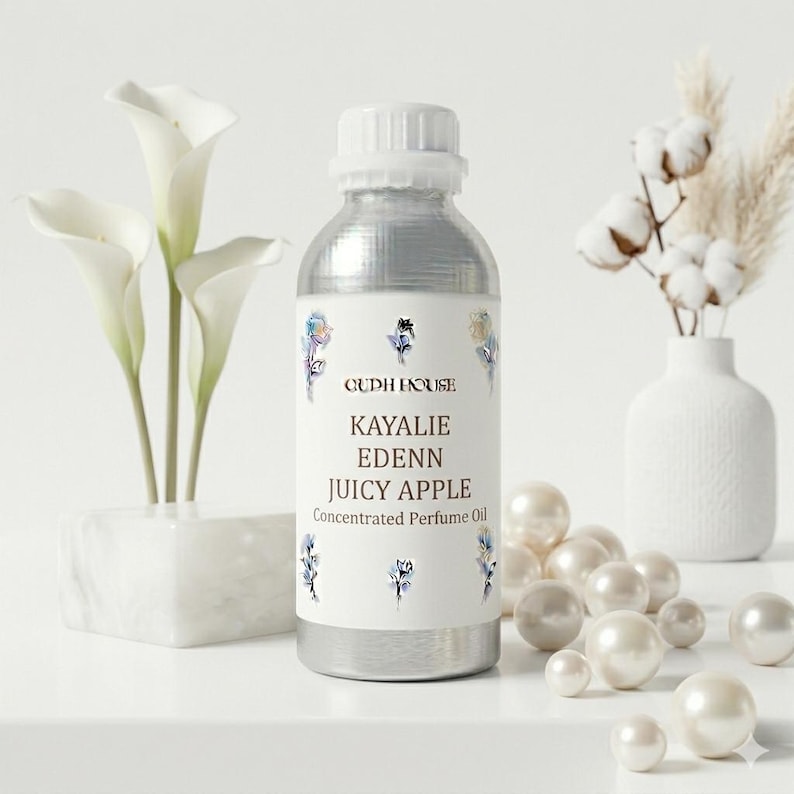 May include: A silver bottle of Kayalie Edenn Juicy Apple concentrated perfume oil. The label features the brand name and product details, with floral accents. White calla lilies and decorative pearls are also in the image.