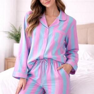 Könnte beinhalten: Zweiteiliger Pyjama mit vertikalen Streifen in Hellblau und Rosa. Das langärmlige Oberteil hat eine Brusttasche und einen Knopfverschluss. Die Hose hat einen Kordelzugbund und Taschen.