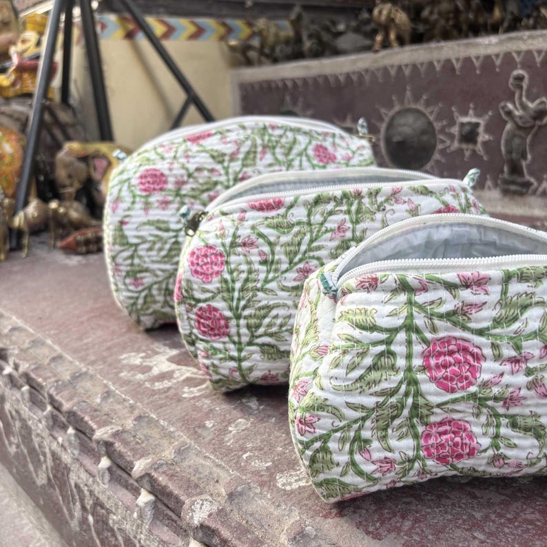 Pode incluir: Tr&ecirc;s bolsas acolchoadas com z&iacute;per de tamanhos variados, cada uma com uma base branca e um padr&atilde;o floral repetitivo de flores rosas e vinhas verdes. As bolsas t&ecirc;m uma apar&ecirc;ncia macia e texturizada com costuras vis&iacute;veis em todo o tecido.