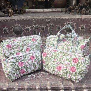 Pode incluir: Um conjunto de tr&ecirc;s bolsas de tecido acolchoado com base branca e um padr&atilde;o repetitivo de flores cor-de-rosa e vinhas verdes. A cole&ccedil;&atilde;o inclui duas bolsas retangulares com fechos e uma mala estruturada com duas al&ccedil;as superiores.