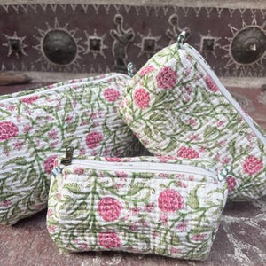 Pode incluir: Tr&ecirc;s bolsas acolchoadas de tamanhos variados com uma base branca e um padr&atilde;o floral repetitivo em tons de rosa e verde. Cada bolsa &eacute; feita de um tecido macio e texturizado e inclui um fecho de correr branco na borda superior.