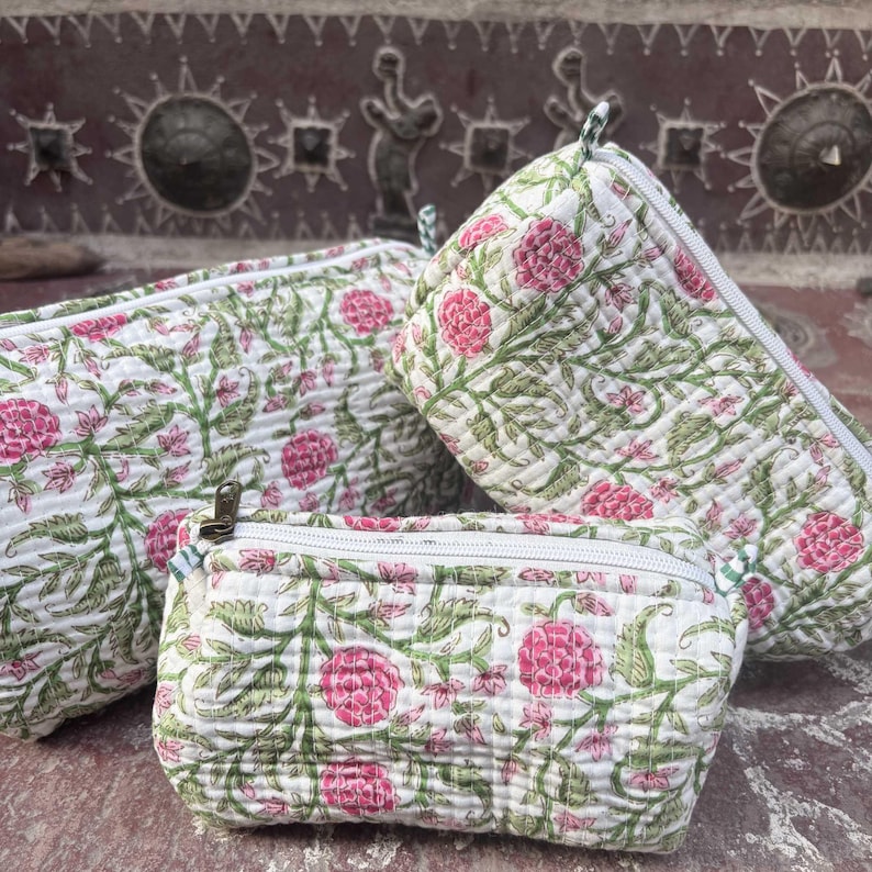 Pode incluir: Tr&ecirc;s bolsas acolchoadas de tamanhos variados com uma base branca e um padr&atilde;o floral repetitivo em tons de rosa e verde. Cada bolsa &eacute; feita de um tecido macio e texturizado e inclui um fecho de correr branco na borda superior.