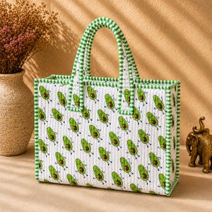 May include: A rectangular quilted tote bag featuring a repeating pattern of cartoon avocados with arms and legs on a white background. The bag has two top handles and edges trimmed with a green and white striped fabric pattern throughout.