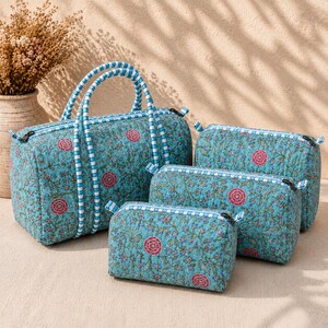 Pode incluir: Um conjunto de quatro bolsas acolchadas de v&aacute;rios tamanhos, em tecido azul-petr&oacute;leo com um padr&atilde;o floral repetitivo de flores cor-de-rosa e vinhas verdes. Cada bolsa tem um fecho &agrave;s riscas azuis e brancas e pegas a condizer na maior.