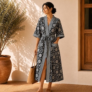 May include: A black and white floral print robe featuring a V-neckline, three-quarter length sleeves, and a matching tie belt. The garment includes vertical striped trim along the front opening, sleeve cuffs, and pockets, reaching a mid-calf length.