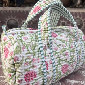 Pode incluir: Uma bolsa acolchoada de formato cil&iacute;ndrico com base branca e um padr&atilde;o floral em tons de rosa e verde. A bolsa inclui duas al&ccedil;as com um design de riscas verdes e brancas e um fecho de correr branco na parte superior.