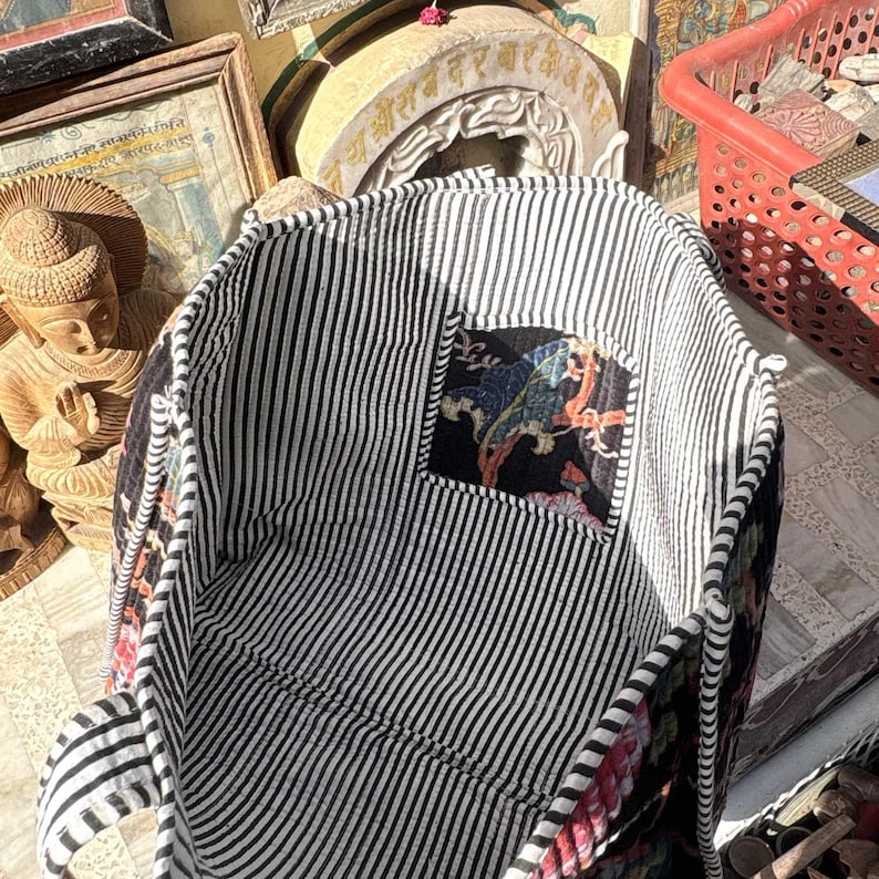 May include: A black and white striped tote bag with a patterned interior pocket. The pocket features a colorful design with birds and floral elements. The bag's handles are also striped, and the bag appears to be made of fabric.