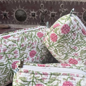 Pode incluir: Tr&ecirc;s bolsas de tecido acolchoado com base branca e um padr&atilde;o floral repetitivo em tons de rosa e verde. Cada bolsa possui um fecho de correr branco com um puxador met&aacute;lico. A textura acolchoada &eacute; vis&iacute;vel em toda a superf&iacute;cie das bolsas.