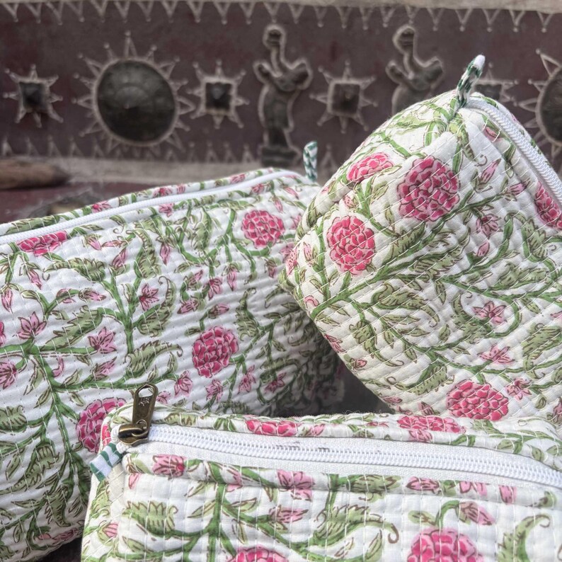 Pode incluir: Tr&ecirc;s bolsas de tecido acolchoado com base branca e um padr&atilde;o floral repetitivo em tons de rosa e verde. Cada bolsa possui um fecho de correr branco com um puxador met&aacute;lico. A textura acolchoada &eacute; vis&iacute;vel em toda a superf&iacute;cie das bolsas.