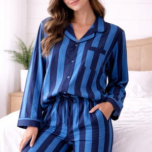 Könnte beinhalten: Blau gestreiftes Pyjama-Set. Das Oberteil hat einen Kragen, eine Knopfleiste und eine Brusttasche. Die Hose hat einen Kordelzug in der Taille und Taschen. Der Pyjama ist aus einem weichen, leichten Stoff gefertigt.