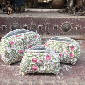 Pode incluir: Um conjunto de tr&ecirc;s bolsas acolchoadas de tamanhos variados, cada uma com uma base de tecido branco com um padr&atilde;o repetitivo de flores cor-de-rosa e vinhas verdes. Cada bolsa tem uma abertura com fecho de correr e um acabamento acolchoado.