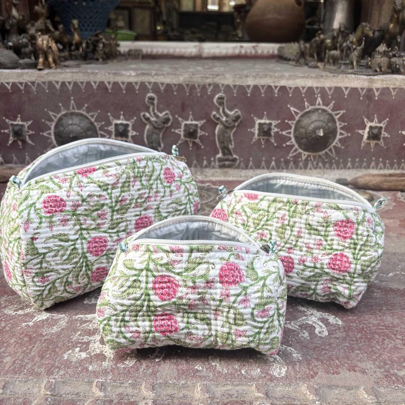Pode incluir: Um conjunto de tr&ecirc;s bolsas acolchoadas de tamanhos variados, cada uma com uma base de tecido branco com um padr&atilde;o repetitivo de flores cor-de-rosa e vinhas verdes. Cada bolsa tem uma abertura com fecho de correr e um acabamento acolchoado.