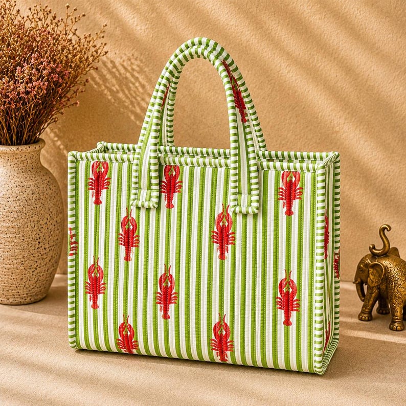 May include: A rectangular tote bag featuring a green and white vertical striped pattern with a repeating red lobster print. The bag has two matching striped top handles and a structured, quilted fabric construction with reinforced edges.