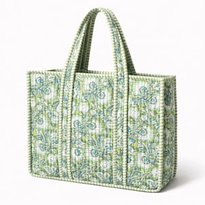 Könnte beinhalten: Eine gesteppte Tragetasche mit einem Blumenmuster in Grün-, Blau- und Weißtönen. Die Tasche hat zwei Griffe und eine rechteckige Form. Die Kanten und Griffe der Tasche sind mit einem hellgrünen Stoff eingefasst.