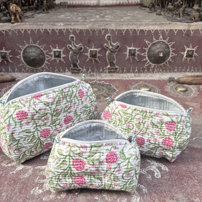 Pode incluir: Tr&ecirc;s n&eacute;cessaires acolchoadas de tamanhos variados, com uma base branca e um padr&atilde;o repetitivo de flores cor-de-rosa e videiras verdes. Cada bolsa possui uma abertura com fecho de correr e um forro interior de cor clara.