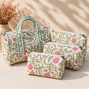 Puede incluir: Un conjunto de cuatro bolsas acolchadas con base blanca y un patrón floral repetitivo de flores rosas y enredaderas verdes. El set incluye una bolsa de viaje grande con dos asas y tres estuches rectangulares más pequeños con cremalleras.