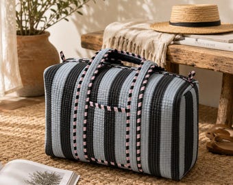 Pode incluir: Mala de viagem retangular com listras verticais pretas e azul claro. A mala tem um pequeno bolso frontal e alças pretas com acabamento rosa e branco. Está sobre um tapete tecido.