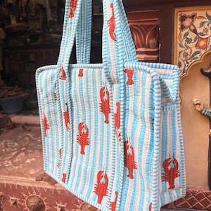 Puede incluir: Un bolso tote acolchado con un patr&oacute;n de rayas azules y blancas y un dise&ntilde;o repetido de langostas rojas. El bolso tiene dos asas resistentes y est&aacute; hecho de un material suave y acolchado. Dise&ntilde;ado para transportar objetos.