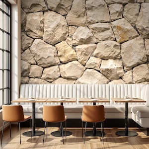 May include: A long white upholstered booth seat positioned against a wall with a light beige stone texture wallpaper. Four square wooden tables with black metal pedestals are arranged in a row, each paired with a tan chair with thin black legs.