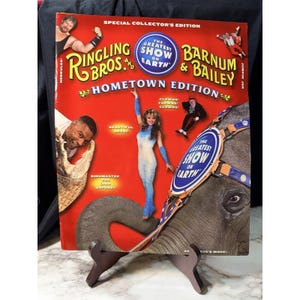 Peut inclure: Une édition collector rouge de Ringling Bros. et Barnum & Bailey Hometown. La couverture présente des artistes de cirque, un éléphant et le texte "The Greatest Show on Earth".