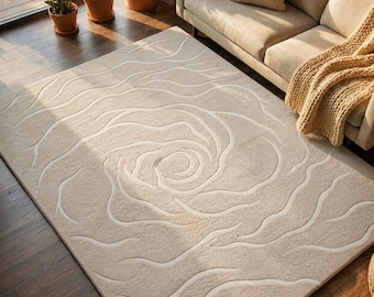 May include: Beige rectangular area rug featuring a large, abstract floral pattern in a lighter beige. The rug is placed on a dark wood floor. The setting is a living room, with a sofa and potted plants visible.