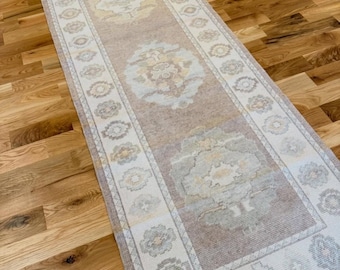 May include: A long, rectangular runner rug featuring a muted colour palette of beige, cream, and soft grey. The rug displays a repeating central medallion pattern and a decorative border with floral motifs, all woven with a low-pile, textured finish.