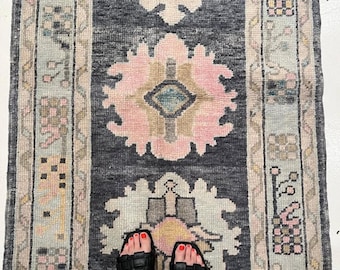 May include: A rectangular runner rug featuring a dark charcoal grey central field with three large, symmetrical floral medallions in shades of soft pink, cream, and muted blue. The rug is framed by wide, light-coloured borders with geometric patterns.