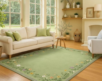 May include: A light green rectangular rug with a floral border. The room features a cream-coloured sofa with green cushions, a wooden side table, and a white armchair. The room has large windows and hardwood flooring.