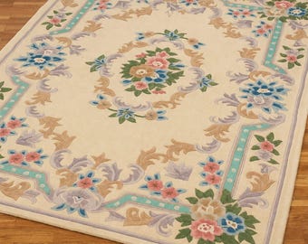May include: Cream-coloured rectangular rug with a floral design. The rug features a central floral medallion surrounded by a border of flowers and scrolling leaves in shades of blue, pink, and tan. The border is outlined in a light teal colour.