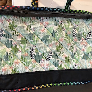 May include: A black zippered tote bag with a green and white tropical print. The bag has a black zipper and a black handle. The bottom of the bag is lined with a rainbow polka dot fabric.