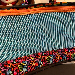 May include: A black zippered tote bag with a blue mesh pocket and a colorful floral print on the bottom. The bag has a rainbow heart pattern on the top.