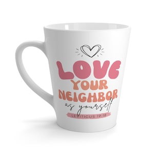 Może przedstawiać: Biały ceramiczny kubek do latte z zakrzywionym uchwytem. Kubek zawiera napis "LOVE YOUR NEIGHBOR as yourself" w kolorze różowym i pomarańczowym, z grafiką serca i wersetem biblijnym Kapłańska 19:18.