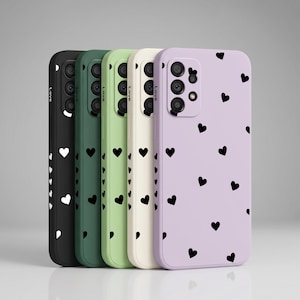 May include: Five smartphone cases arranged in a row, featuring black, dark green, light green, cream, and lavender colors. Each case displays a repeating pattern of small black hearts and the word Love printed on the side edge near the camera lens.