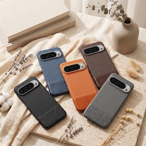 May include: Five smartphone cases in black, blue, orange, brown, and grey. Each case features a textured fabric upper section and a smooth, solid-coloured lower section, with a horizontal camera cutout at the top containing multiple lenses.