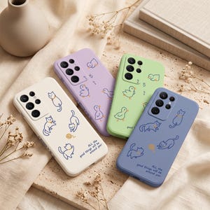 Könnte beinhalten: Vier Smartphone-Hüllen in Creme, Lavendel, Hellgrün und Blau. Die cremefarbene und die blaue Hülle zeigen Katzenillustrationen und den Text 'ALL the good things will be around you'. Die lavendelfarbene und grüne Hülle zeigen kleine Enten.