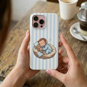May include: A light blue and white striped phone case featuring a cartoon illustration of a monkey in pajamas hugging a teddy bear. The monkey is lying in a woven basket. The phone case has a camera cutout.