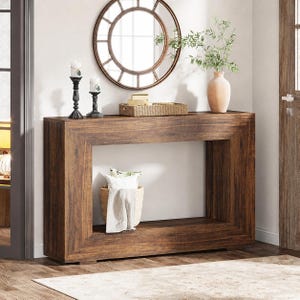 May include: A dark brown wooden console table with a rectangular frame. A round mirror hangs above the table, and decorative items like candles, a basket, and a vase are displayed on top. A basket with a blanket and pillows sits below.